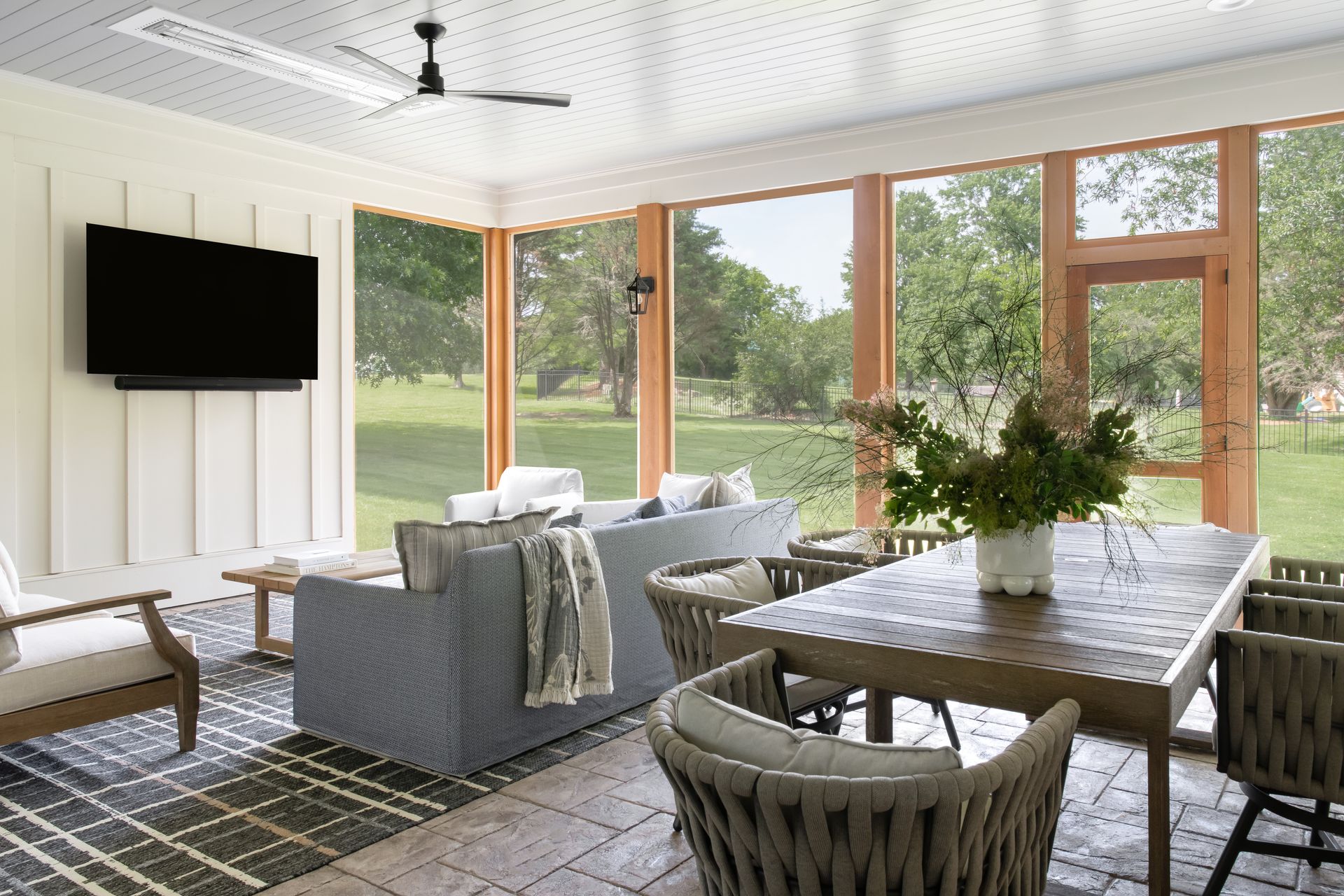 Sunroom with a TV, couch, and dining table overlooking a green yard.