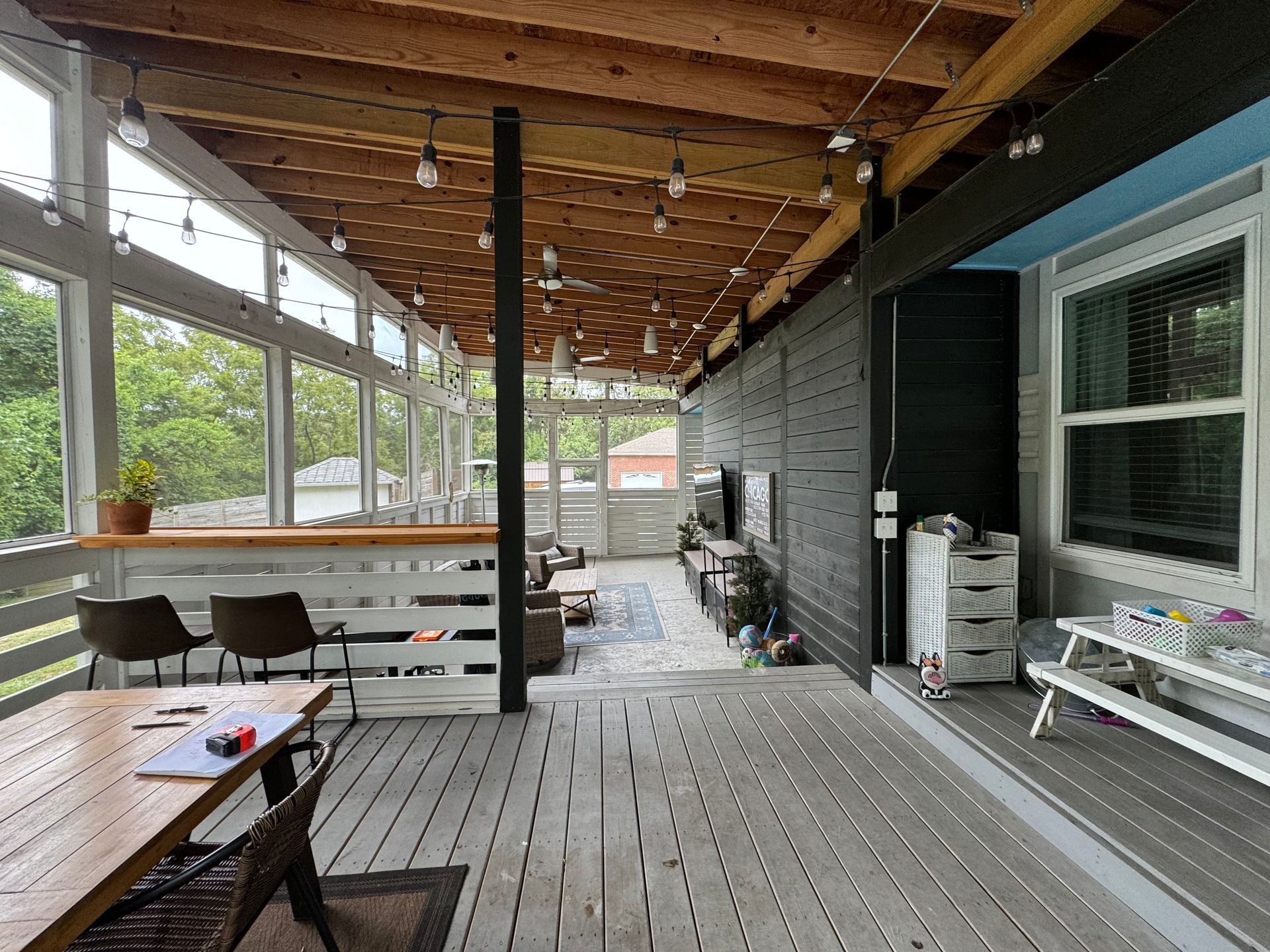 Outdoor deck with string lights, seating, and a table next to a house with a view.