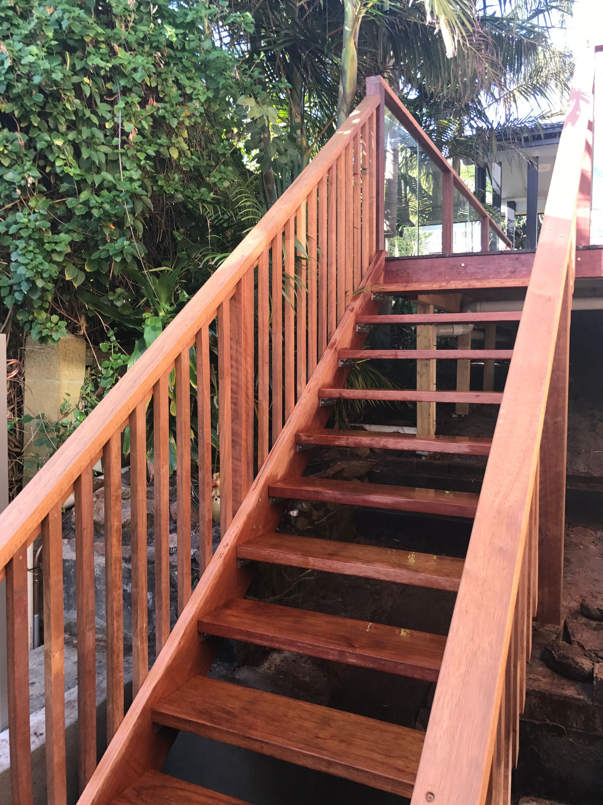 Wooden outdoor staircase leading up to a deck, surrounded by greenery.