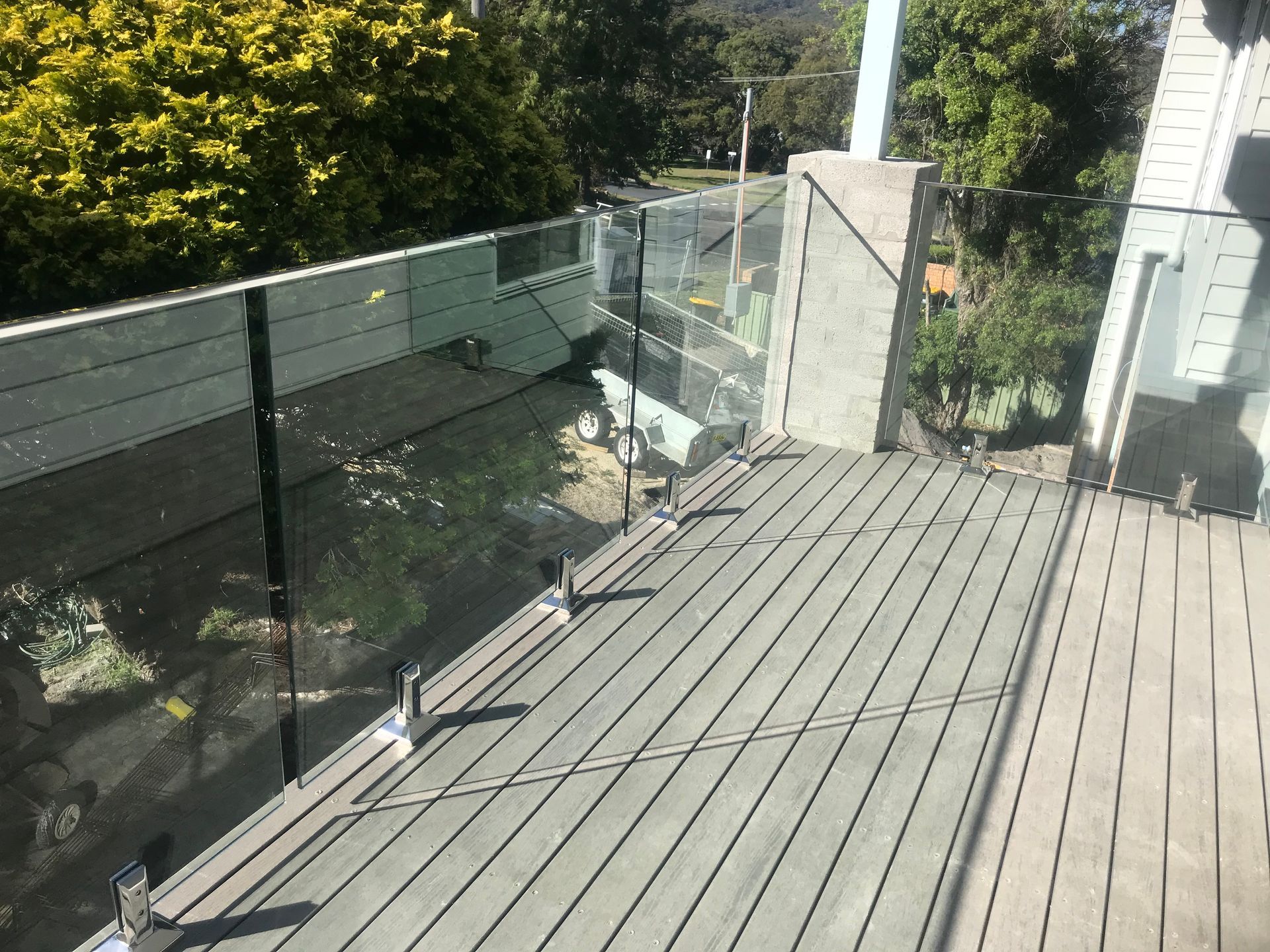 Deck with glass railing overlooking greenery.