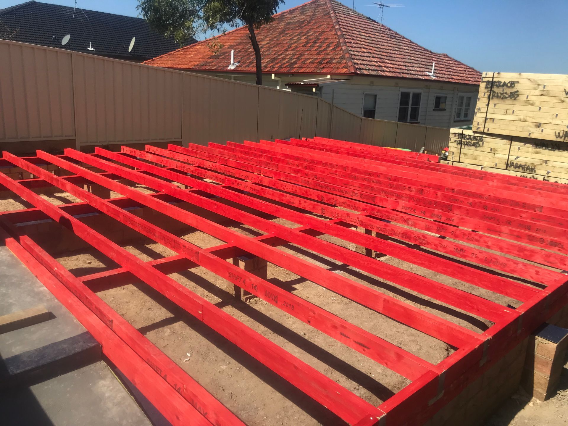 Red-painted wooden deck frame on a dirt surface, with a house and fence in the background — Keystone Property Solutions In Maitland, NSW
