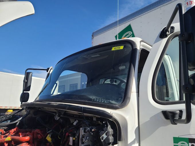 White delivery truck with open hood and door, parked outdoors under a blue sky