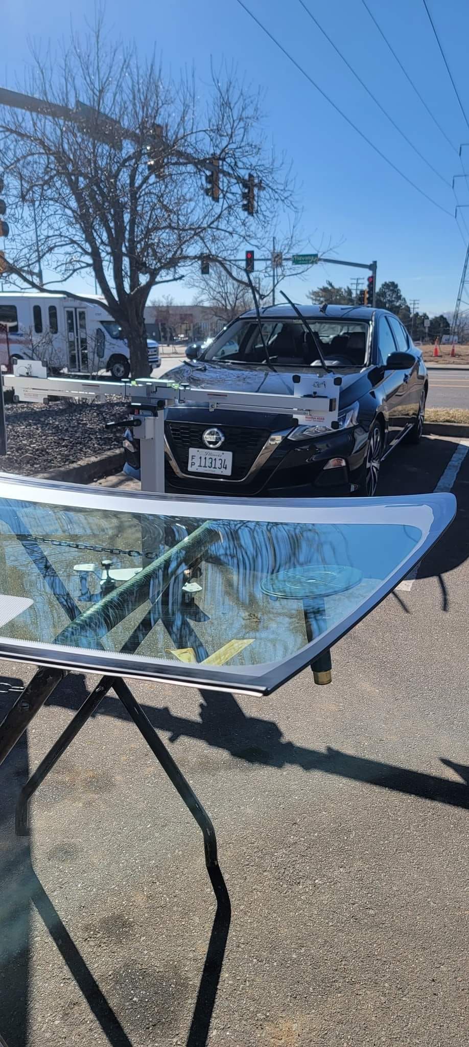Damaged car with shattered windshield on a gravel lot beside a snowy roadside under blue sky