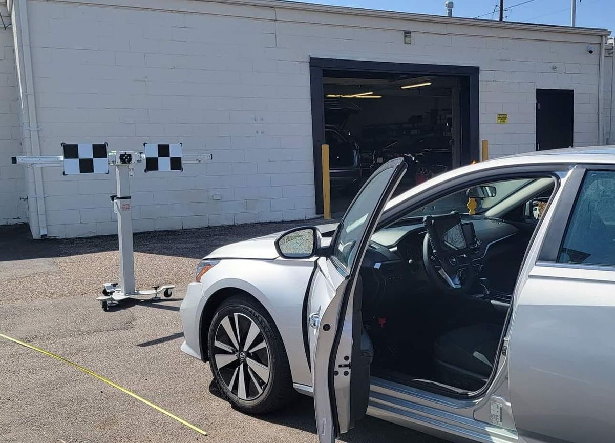 Silver car with driver door open in front of a white building and garage bay