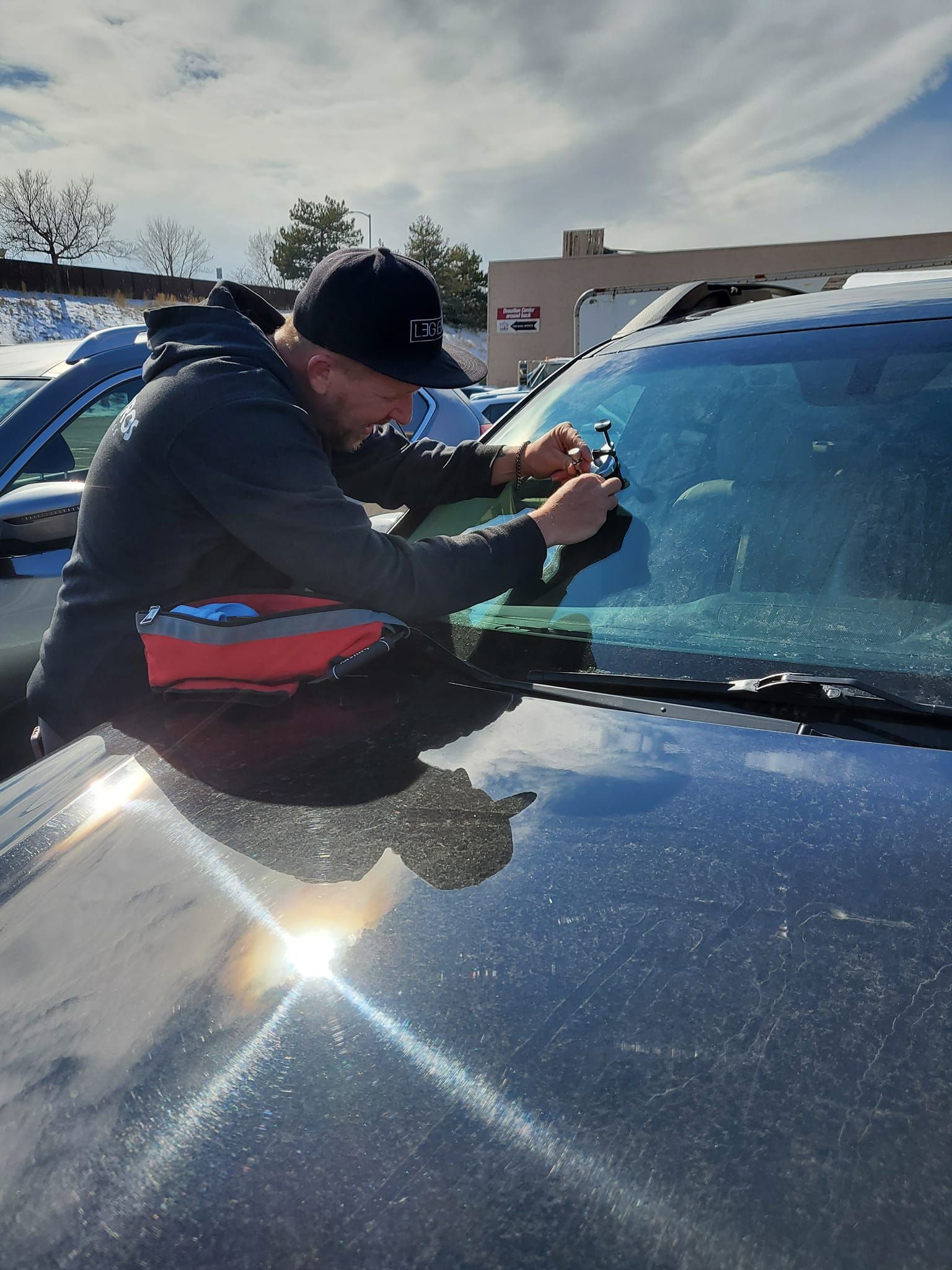 Person scraping ice off a black car windshield on a sunny day.