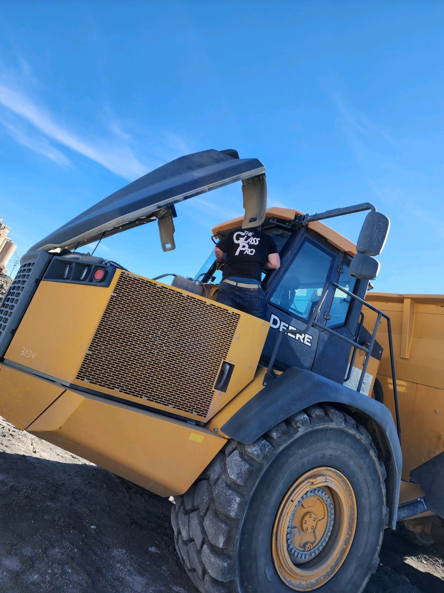 Blue-and-yellow construction loader on gravel, with a person in the cab and the front bucket raised under a blue sky