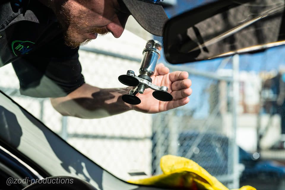 Mechanic using a suction-cup tool near a car windshield in a garage