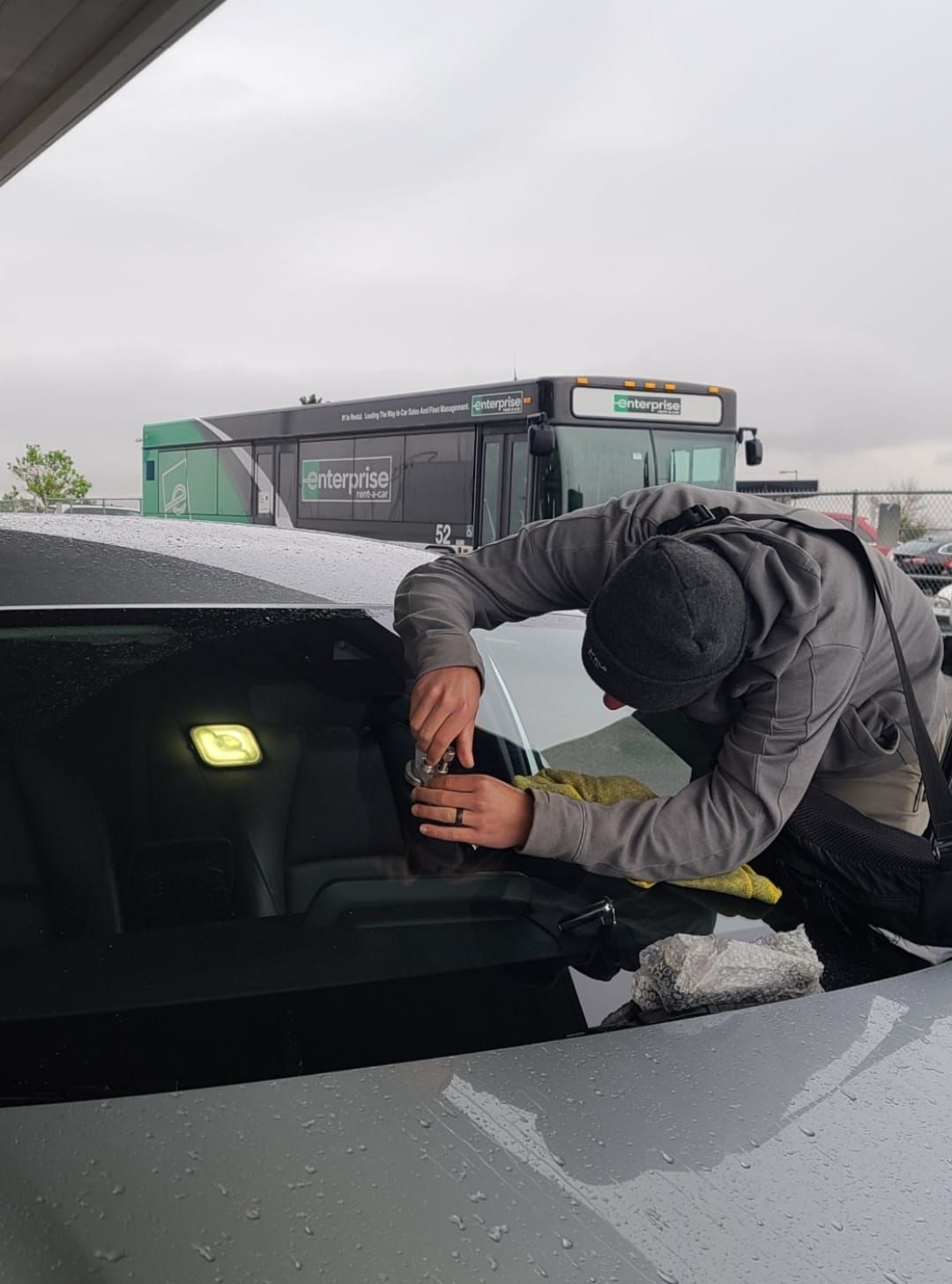Person leaning into a car windshield opening in a snowy parking lot, tightening or repairing something.