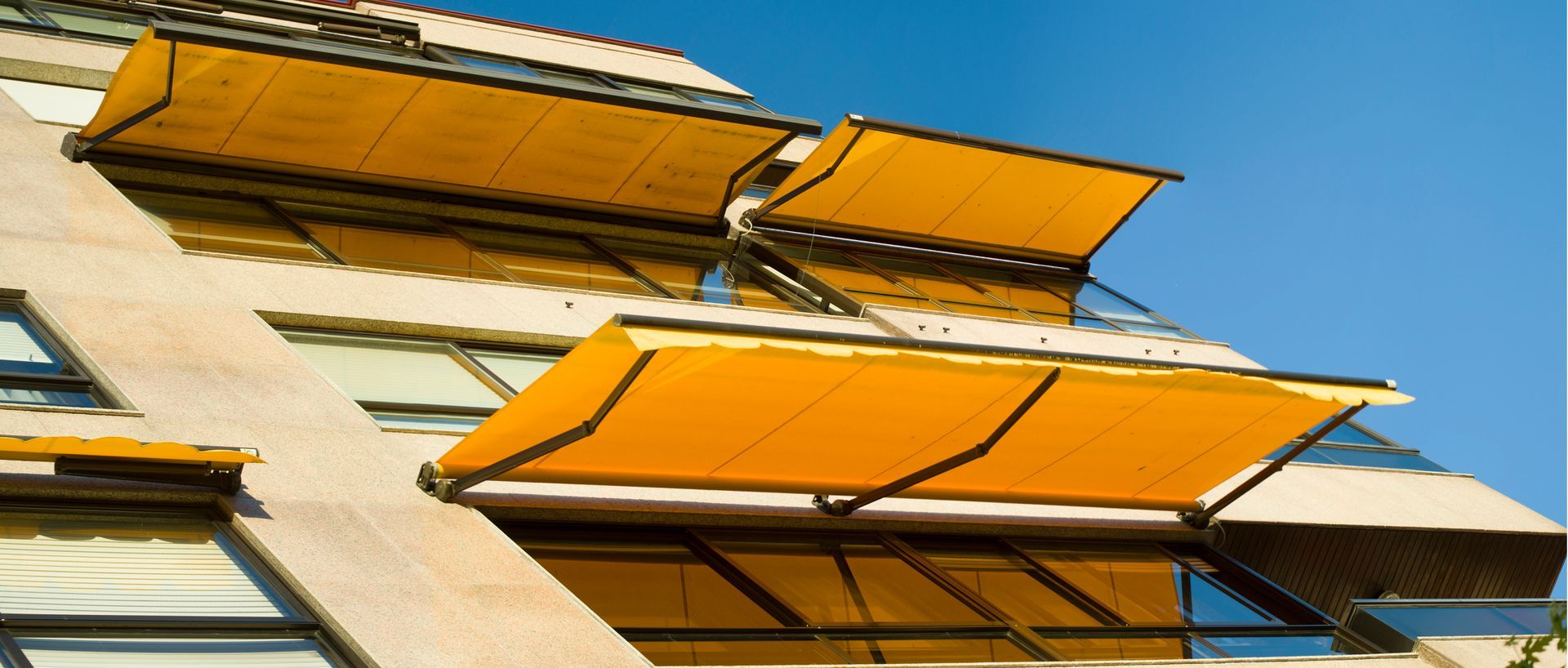 A multi-story building facade featuring slanted concrete walls and bright yellow retractable window awnings.