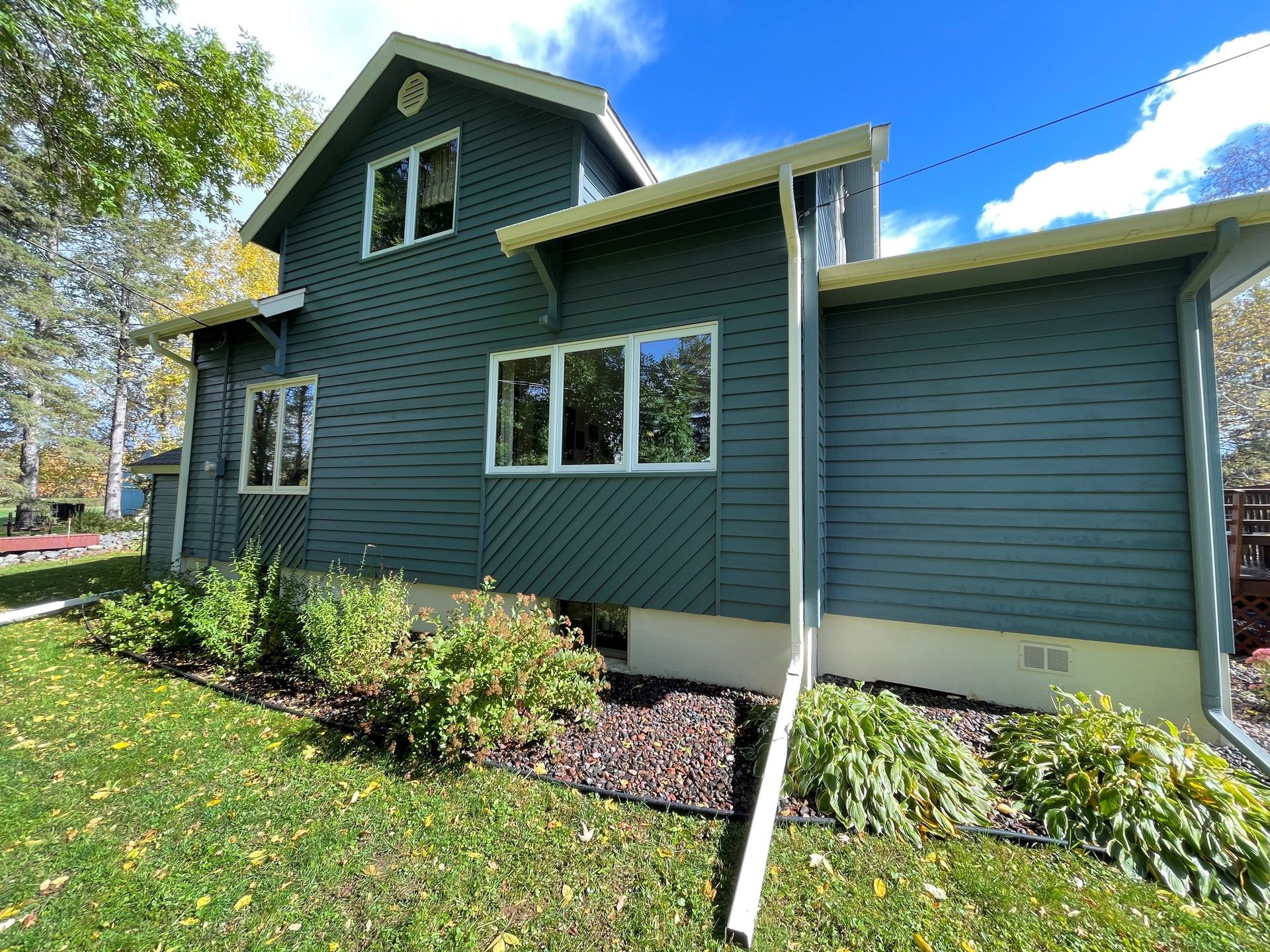 A two-story house with dark blue horizontal siding, white trim, and a cream-colored foundation, set against a blue sky.