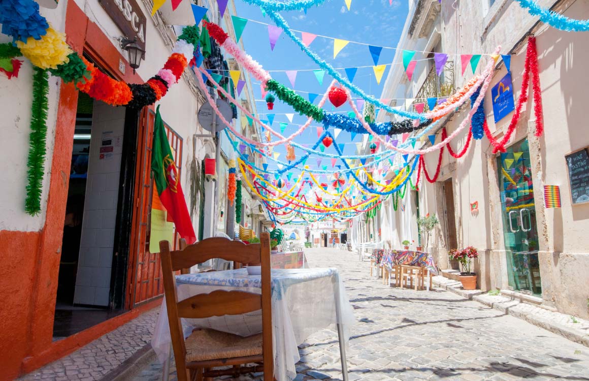 Uma rua estreita com mesas e cadeiras decoradas para um festival.