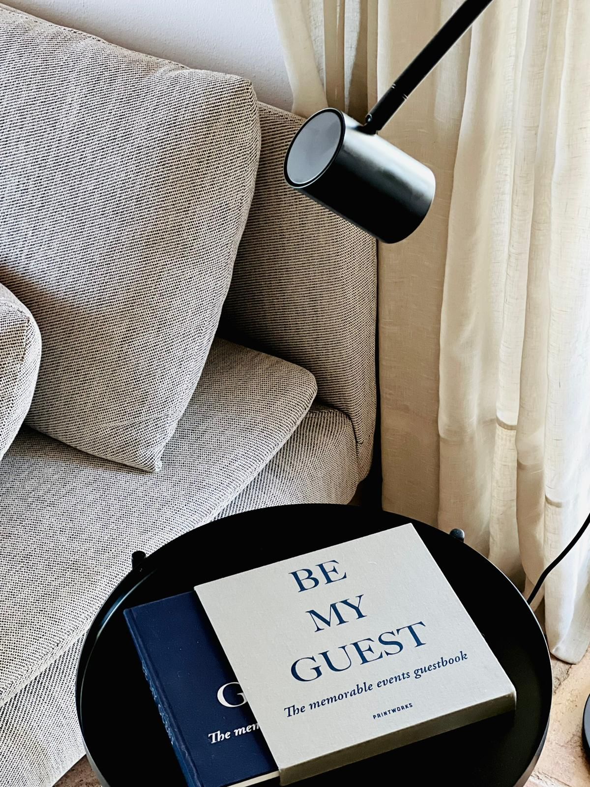 Ein Buch mit dem Titel „Sei mein Gast“ liegt auf einem Tisch neben einem Sofa.