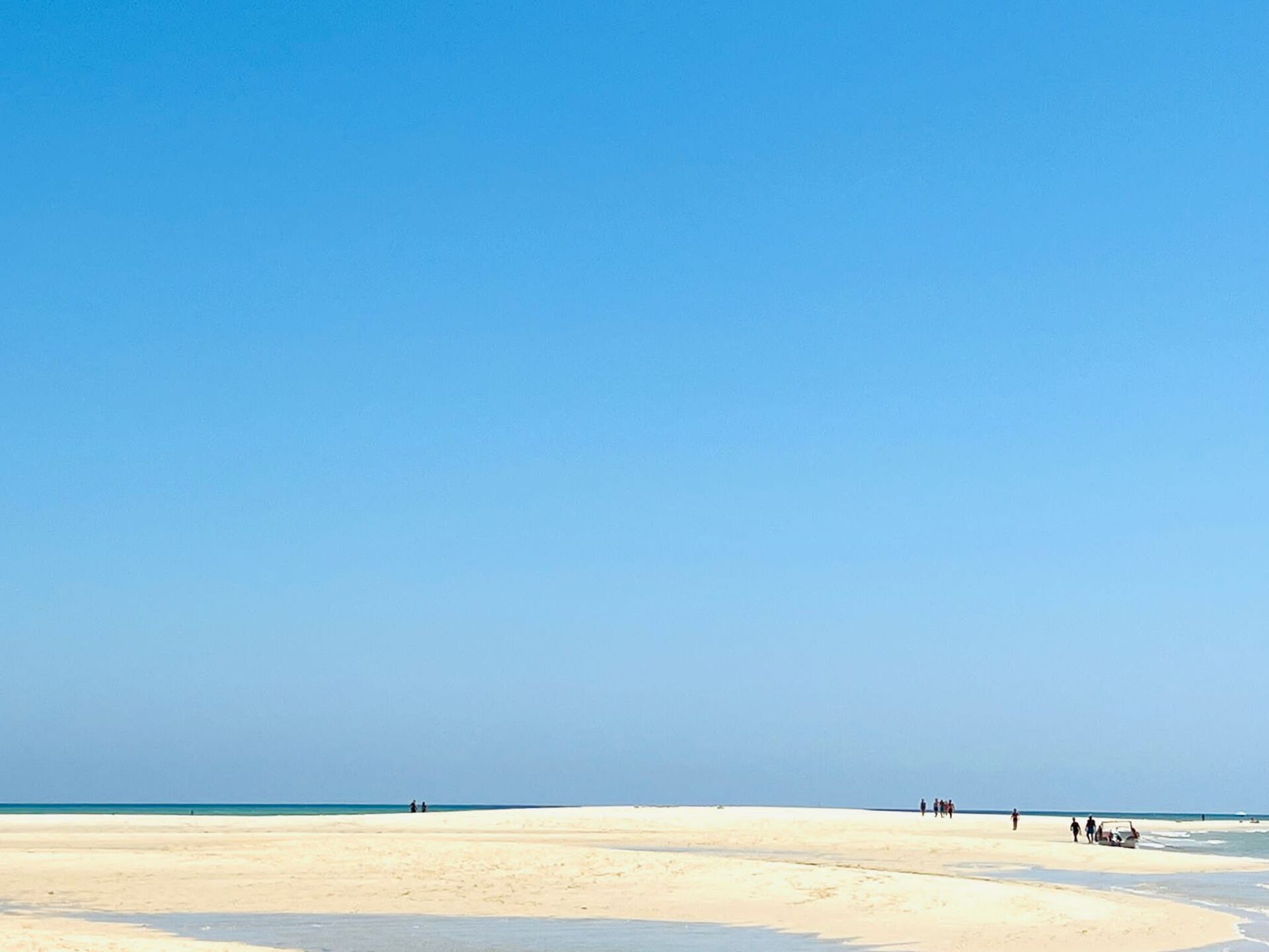 Um grupo de pessoas está caminhando em uma praia arenosa perto do oceano.