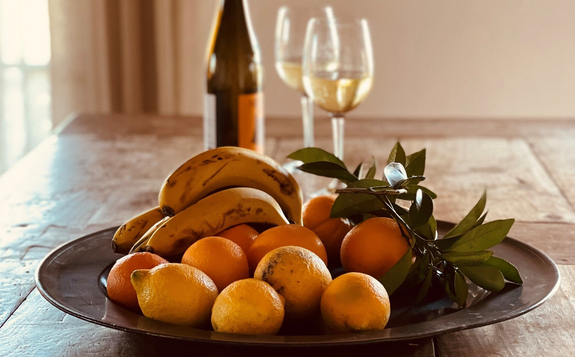 Eine Schale mit Obst steht neben einer Flasche Wein auf einem Holztisch.