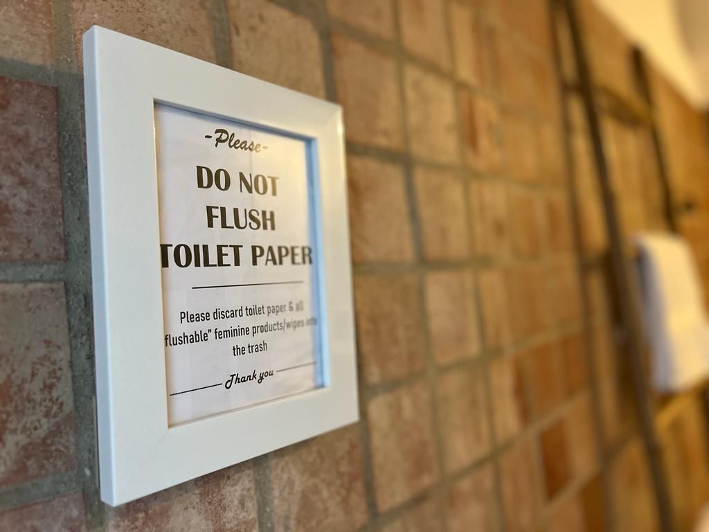 An der Wand hängt ein Schild mit der Aufschrift „Kein Toilettenpapier in die Toilette werfen“.