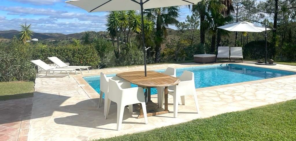Een zwembad met een tafel en stoelen onder een parasol.