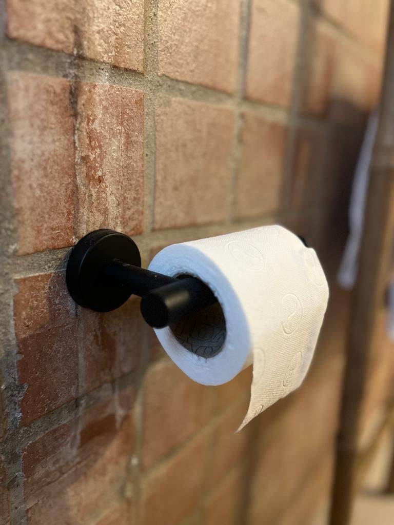 Eine Rolle Toilettenpapier hängt an einem schwarzen Toilettenpapierhalter an einer Ziegelwand.