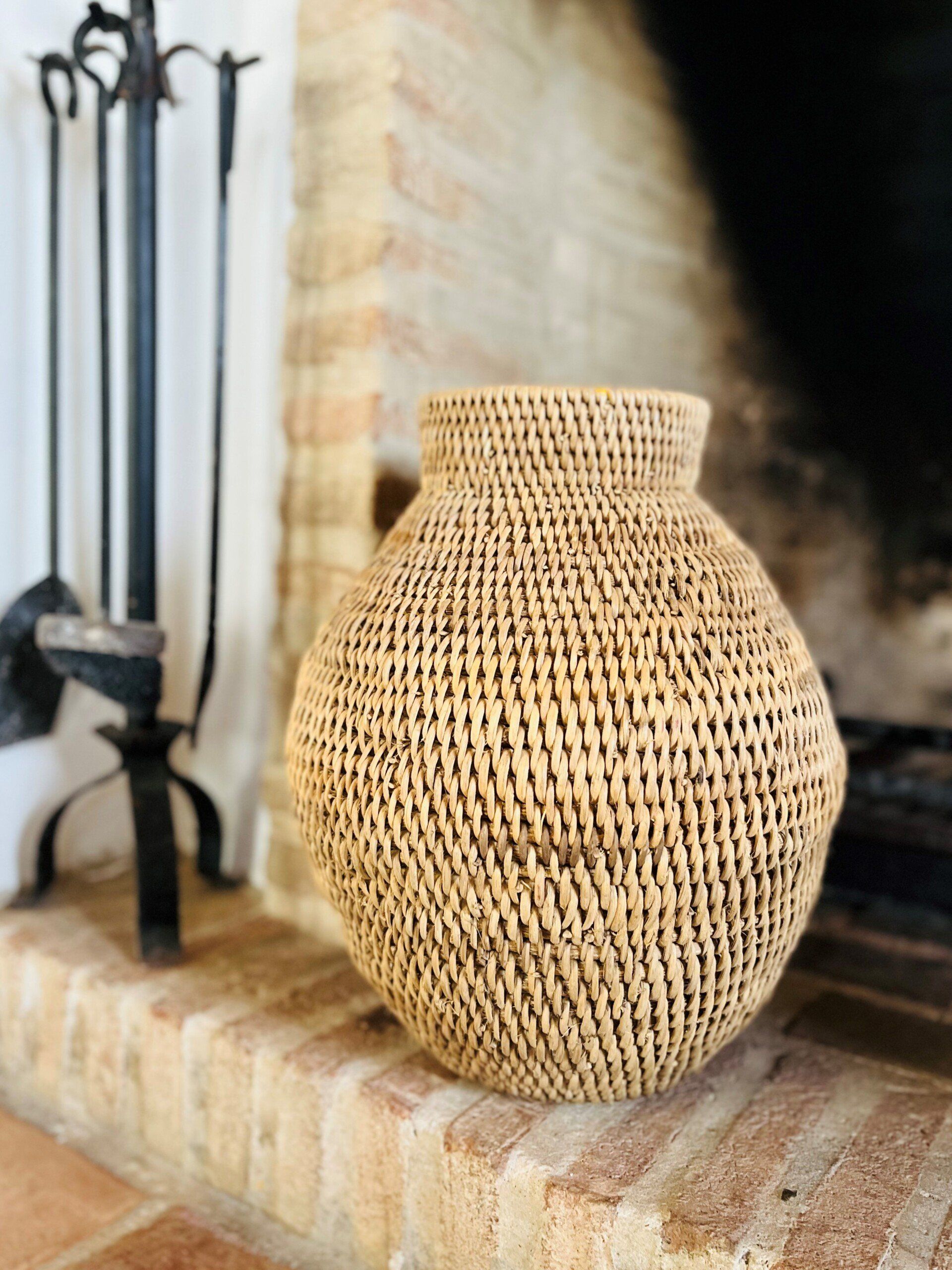 Eine Korbvase steht auf einem gemauerten Kamin neben einem Kamin.