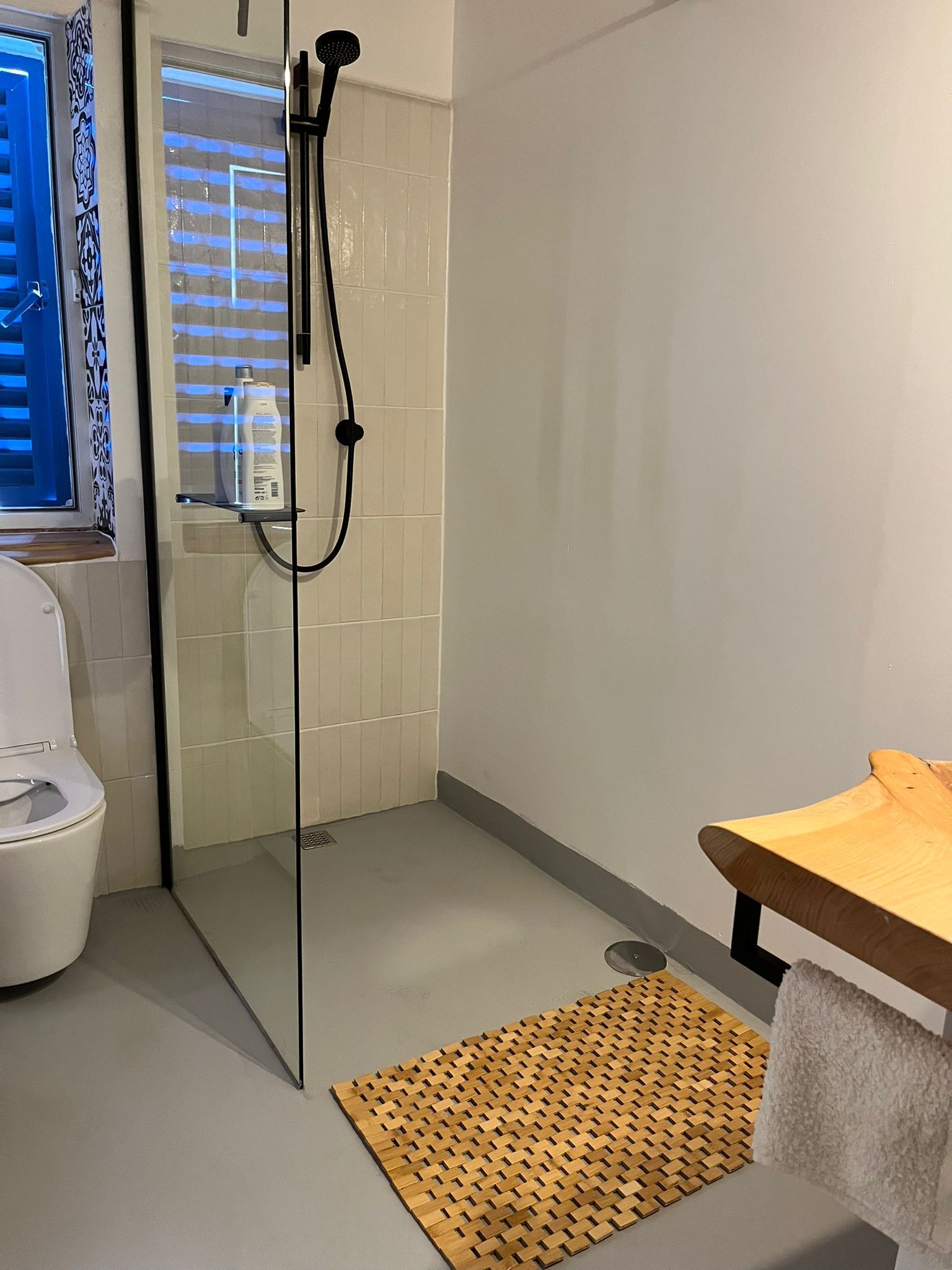 Ein Badezimmer mit ebenerdiger Dusche, Toilette, Waschbecken und Fenster.