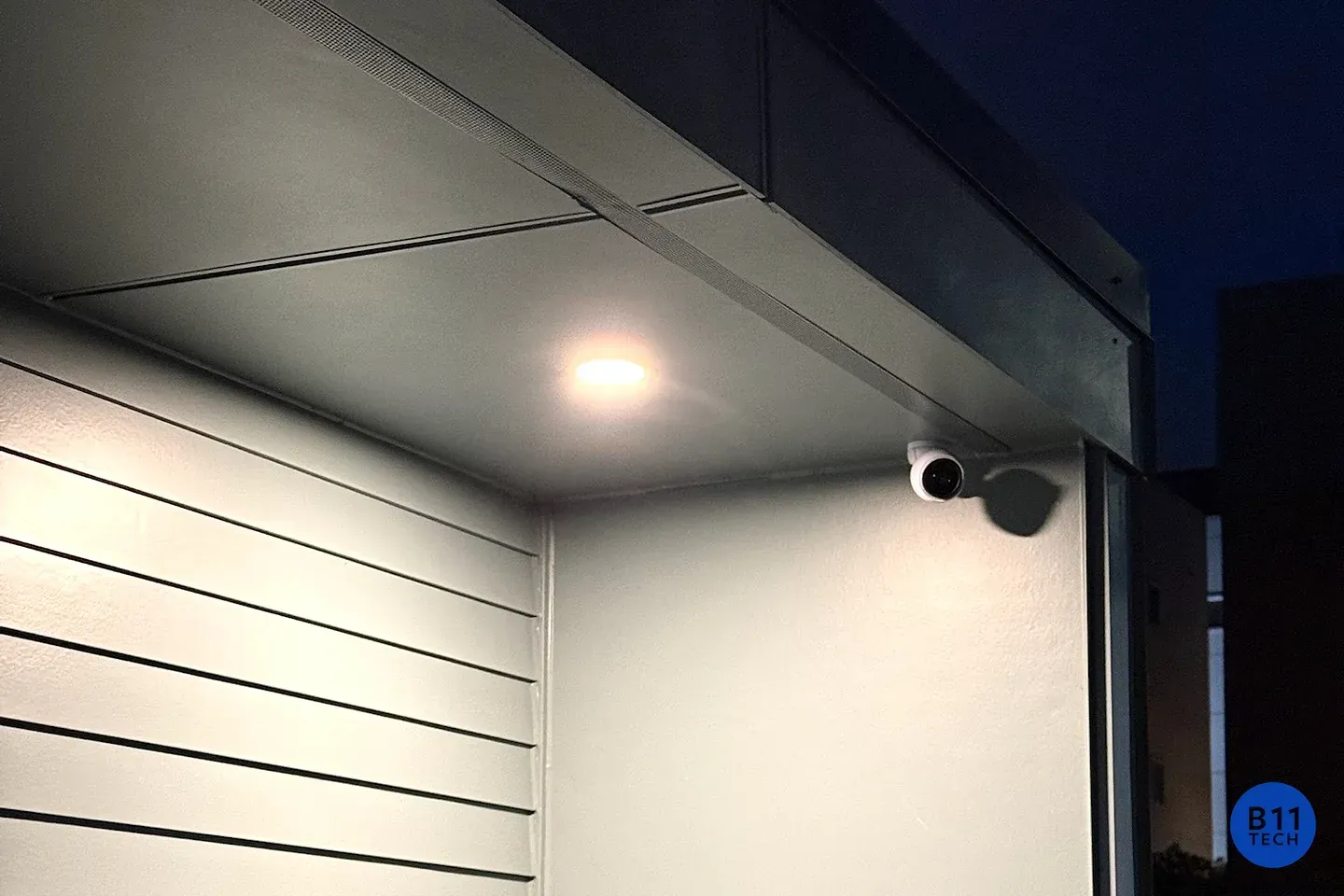 An exterior security camera beside an illuminated entry, photographed by B11 Tech.