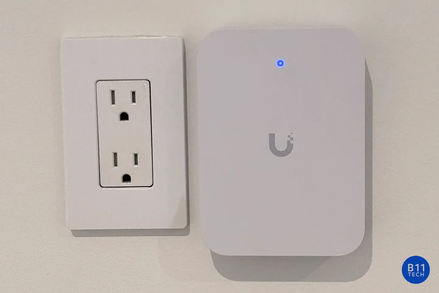 A wall-mounted UniFi access point with its status light illuminated, photographed at a B11 Tech installation