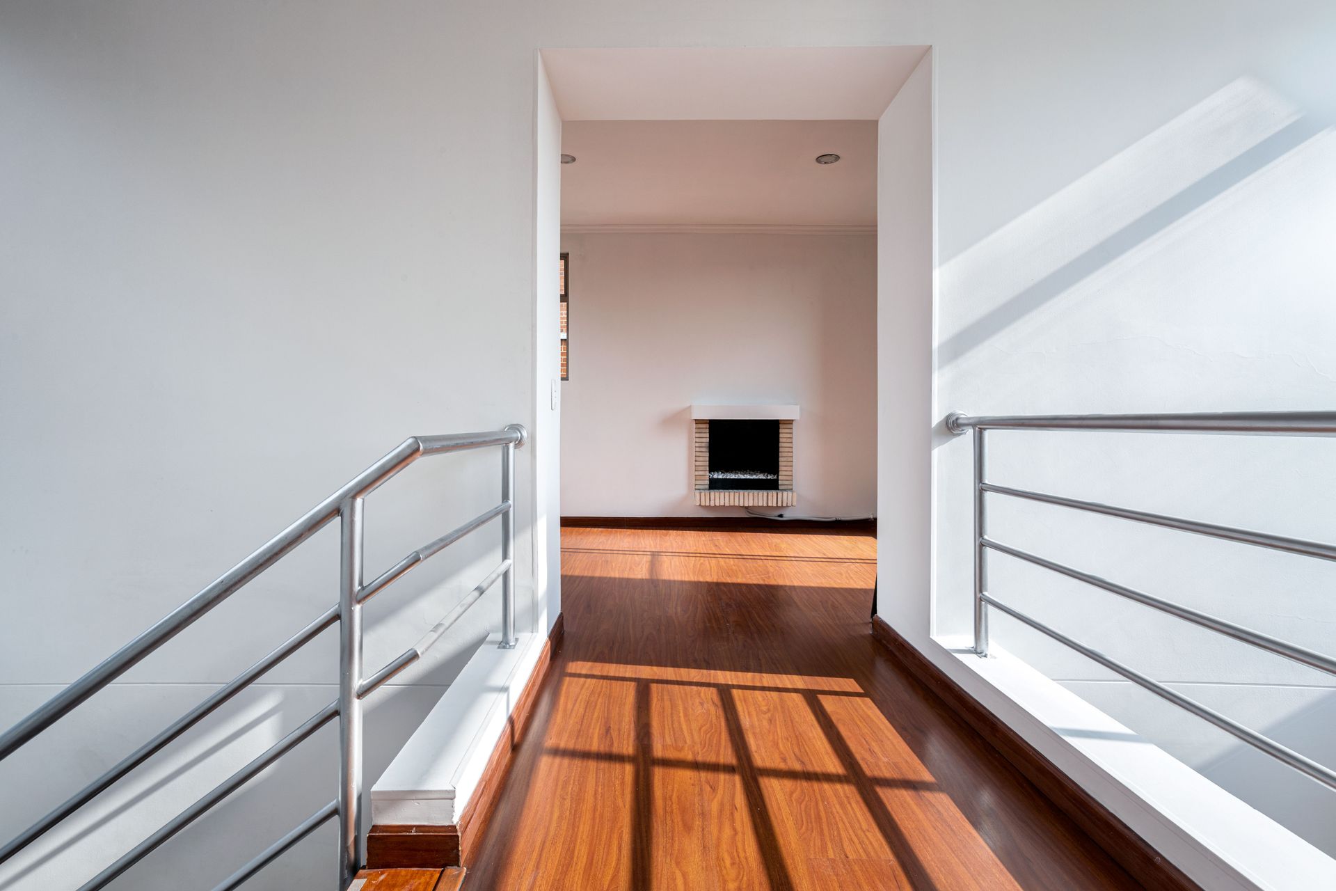Bright hallway with metal railings leading to a sunlit room and TV at the far end