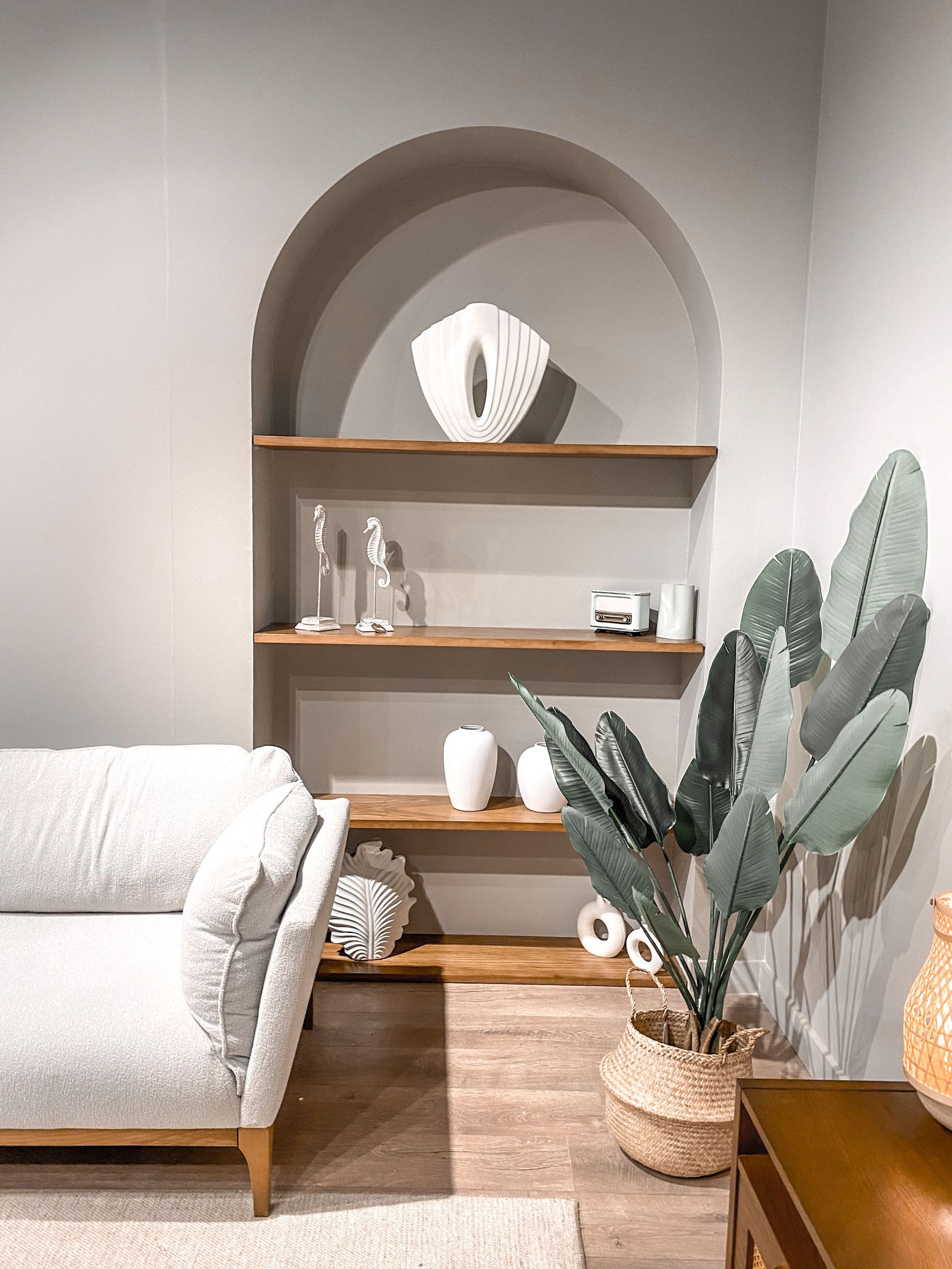 Cozy corner with arched shelf, white sofa, and tall potted plant in a neutral living room.