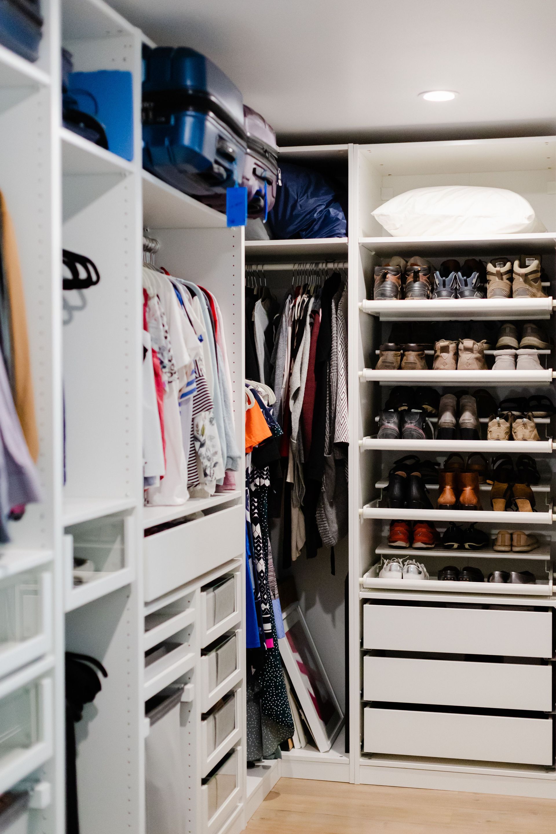 Walk-in closet with white shelves, drawers, hanging clothes, and neatly arranged shoes and bags