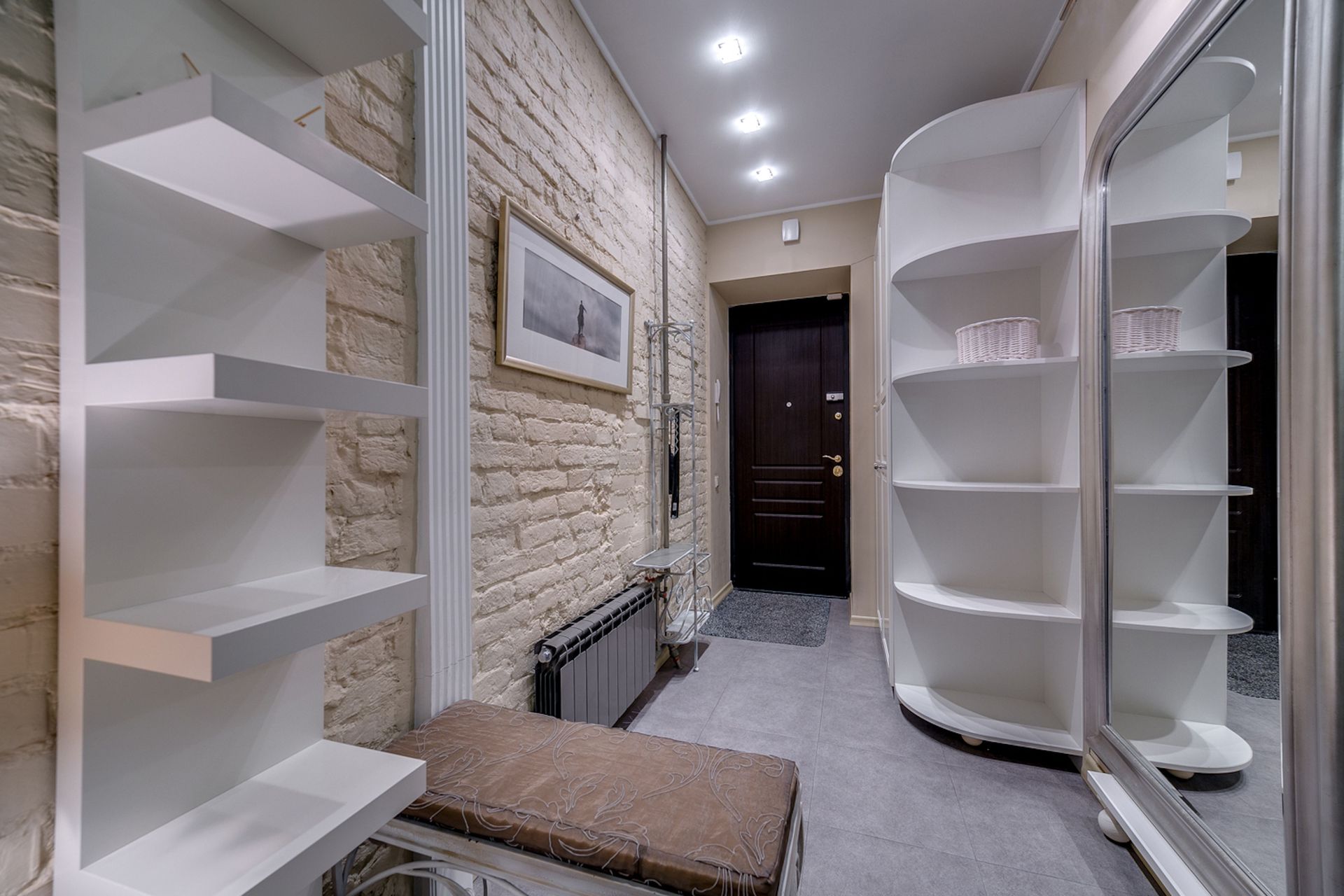Narrow walk-in closet with white shelves, mirrored wall, stone accent wall, and a bench