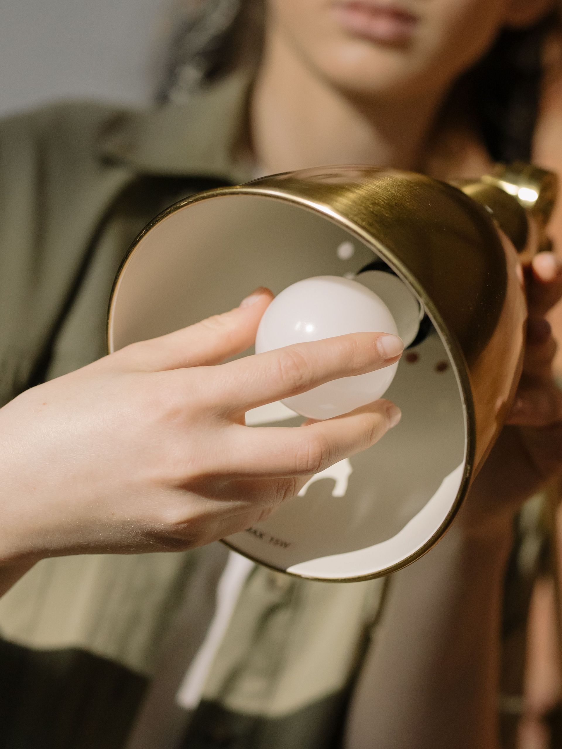 Hand placing a light bulb into a brass lamp shade