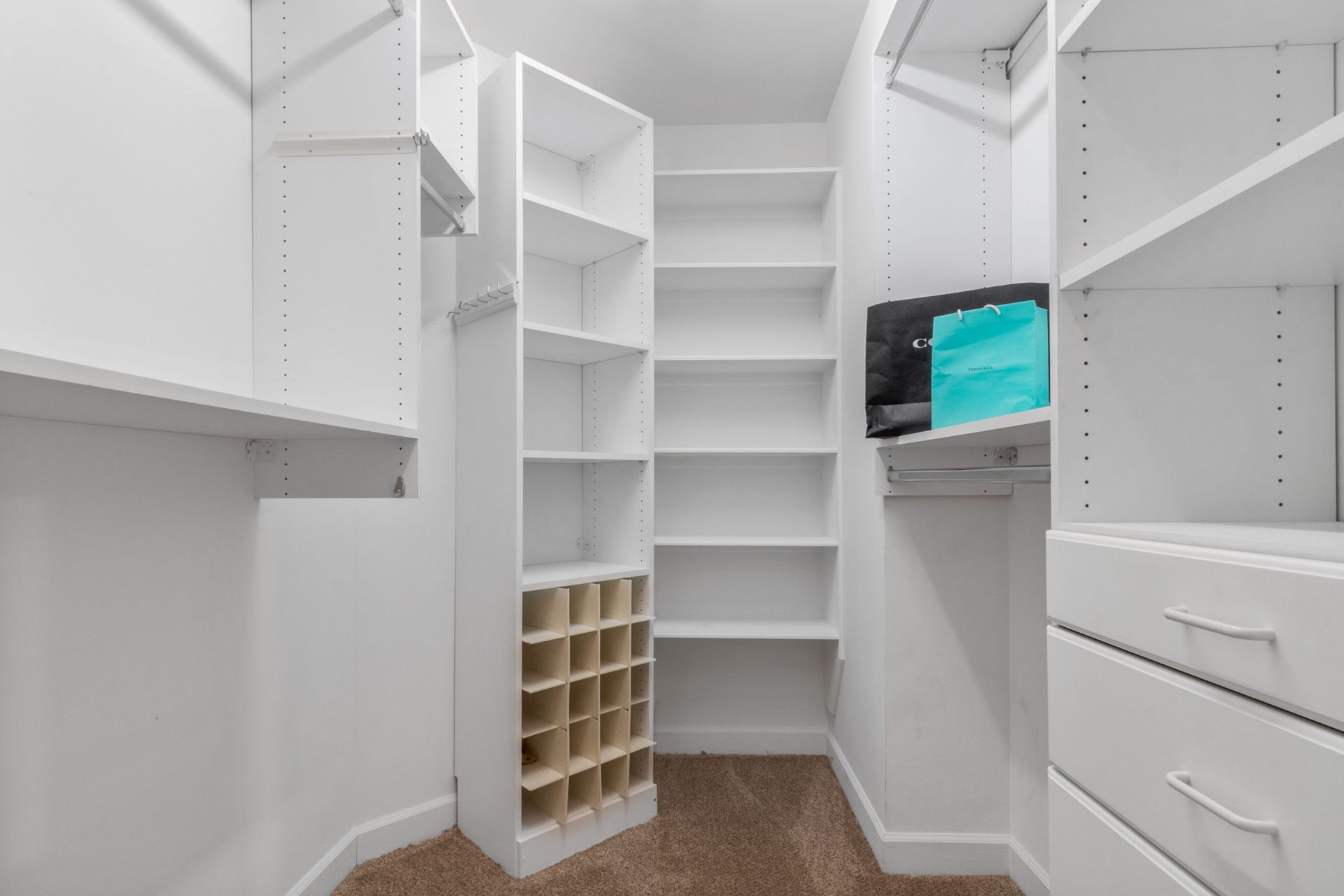 White walk-in closet with built-in shelves, drawers, and cubbies; a small screen sits on one shelf.