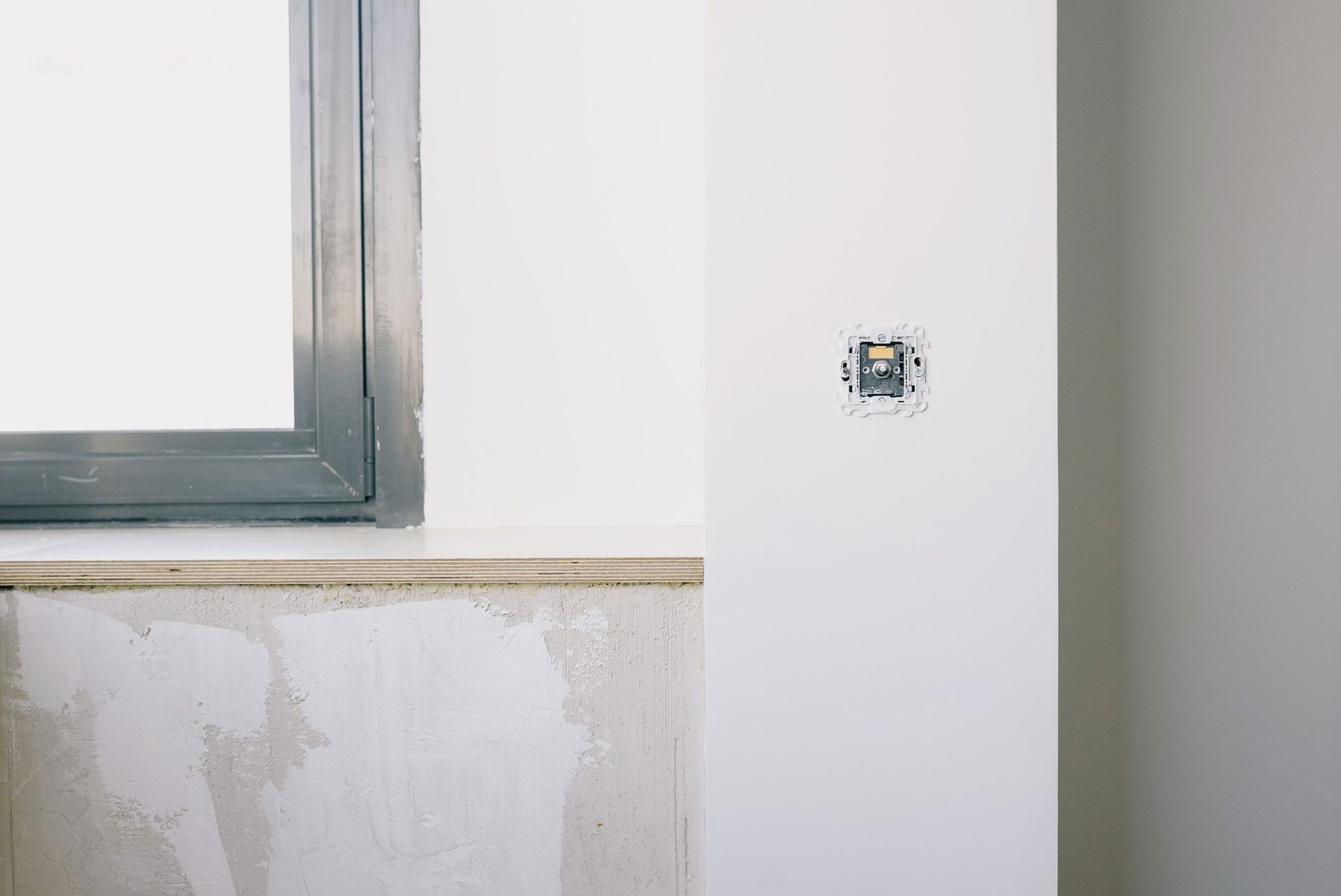 Partially finished wall beside a window, with exposed patching and a small outlet opening.