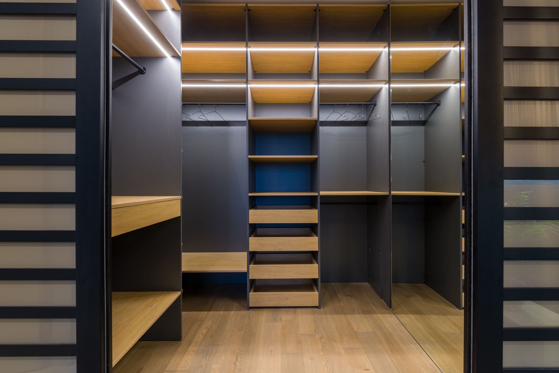 Built-in walk-in closet with wood shelves, dark panels, and warm LED lighting