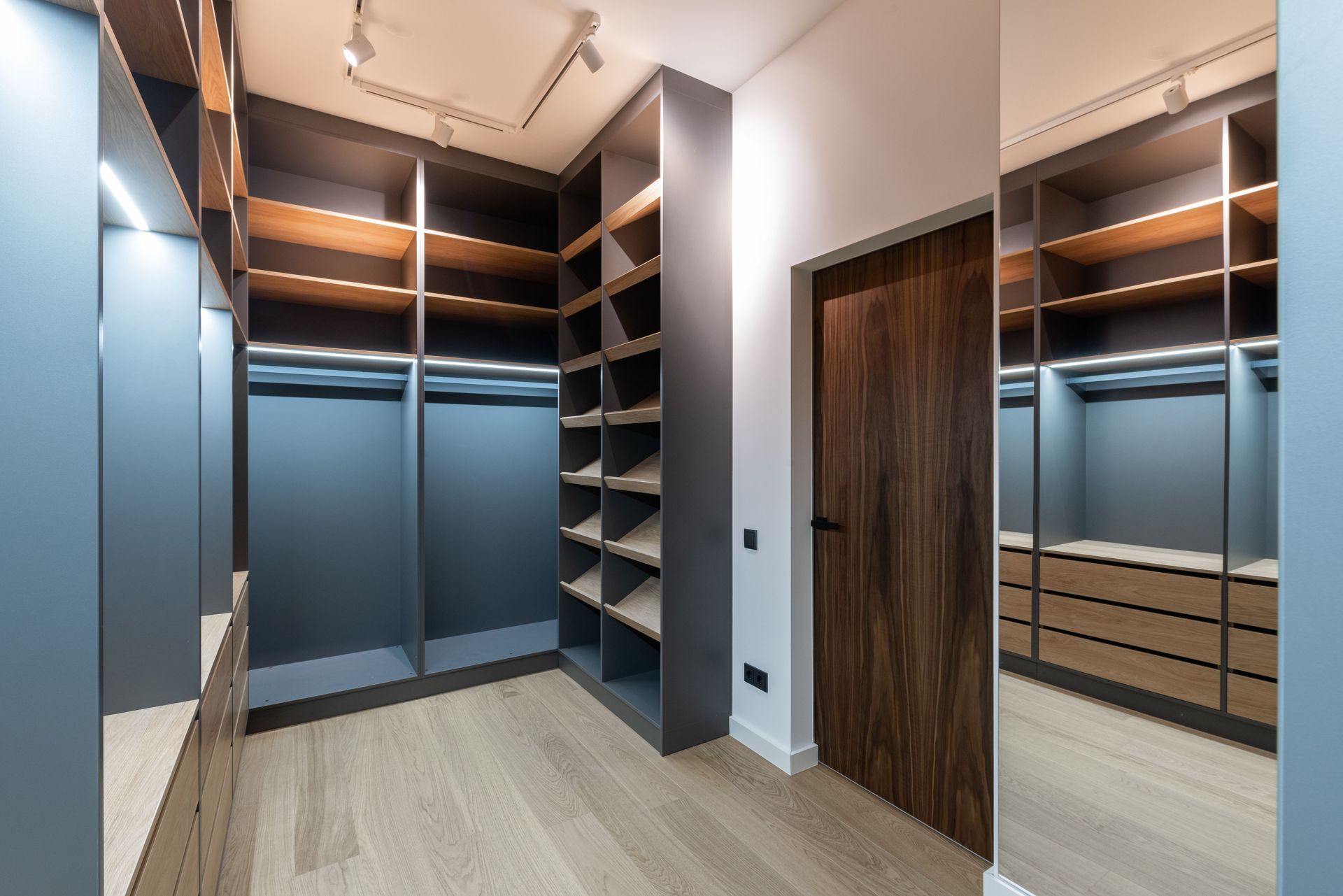Empty walk-in closet with built-in shelving, hanging rods, blue drawers, wood floor, and a wood door