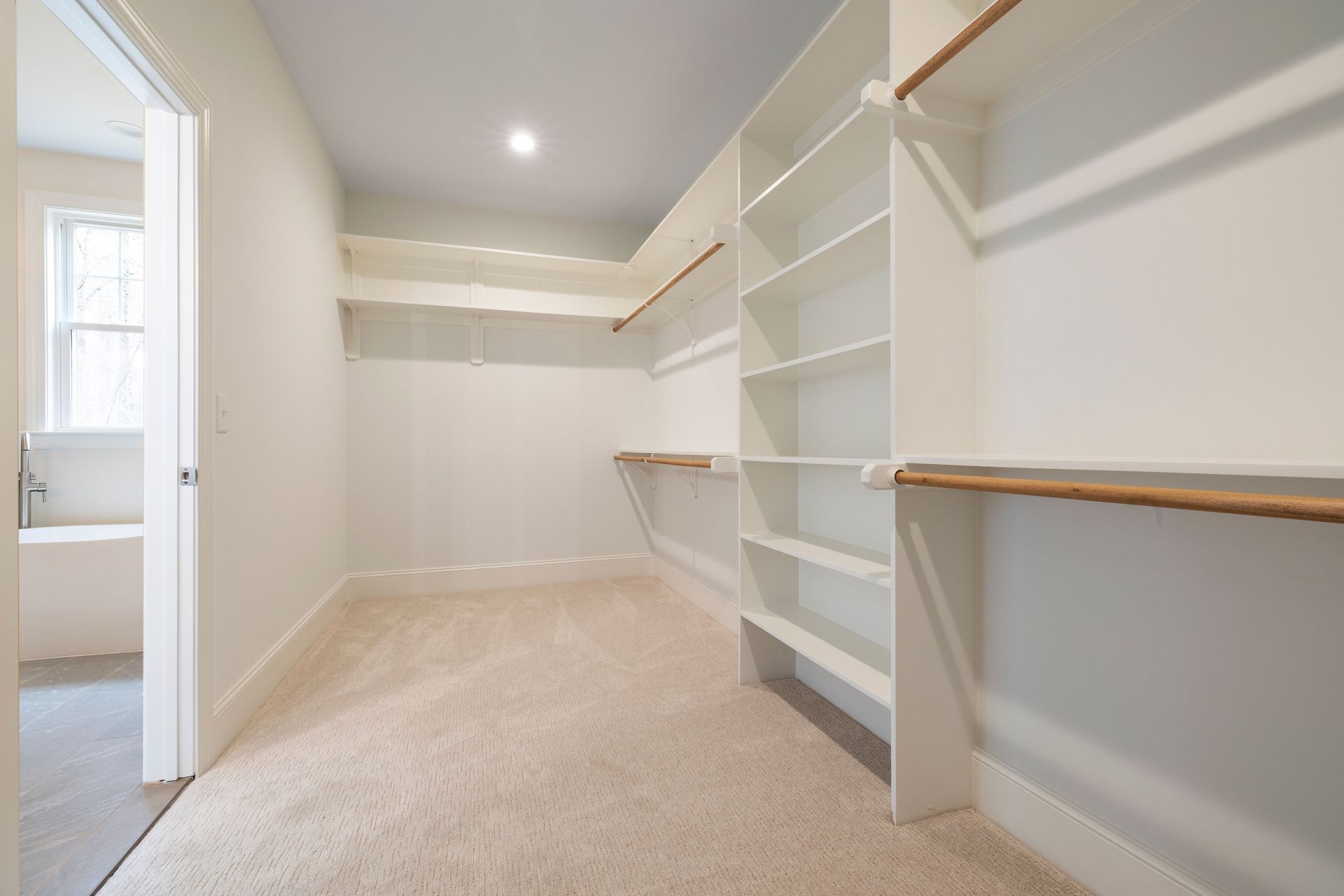 Walk-in closet with white built-in shelves, hanging rods, and beige carpet, viewed from the doorway