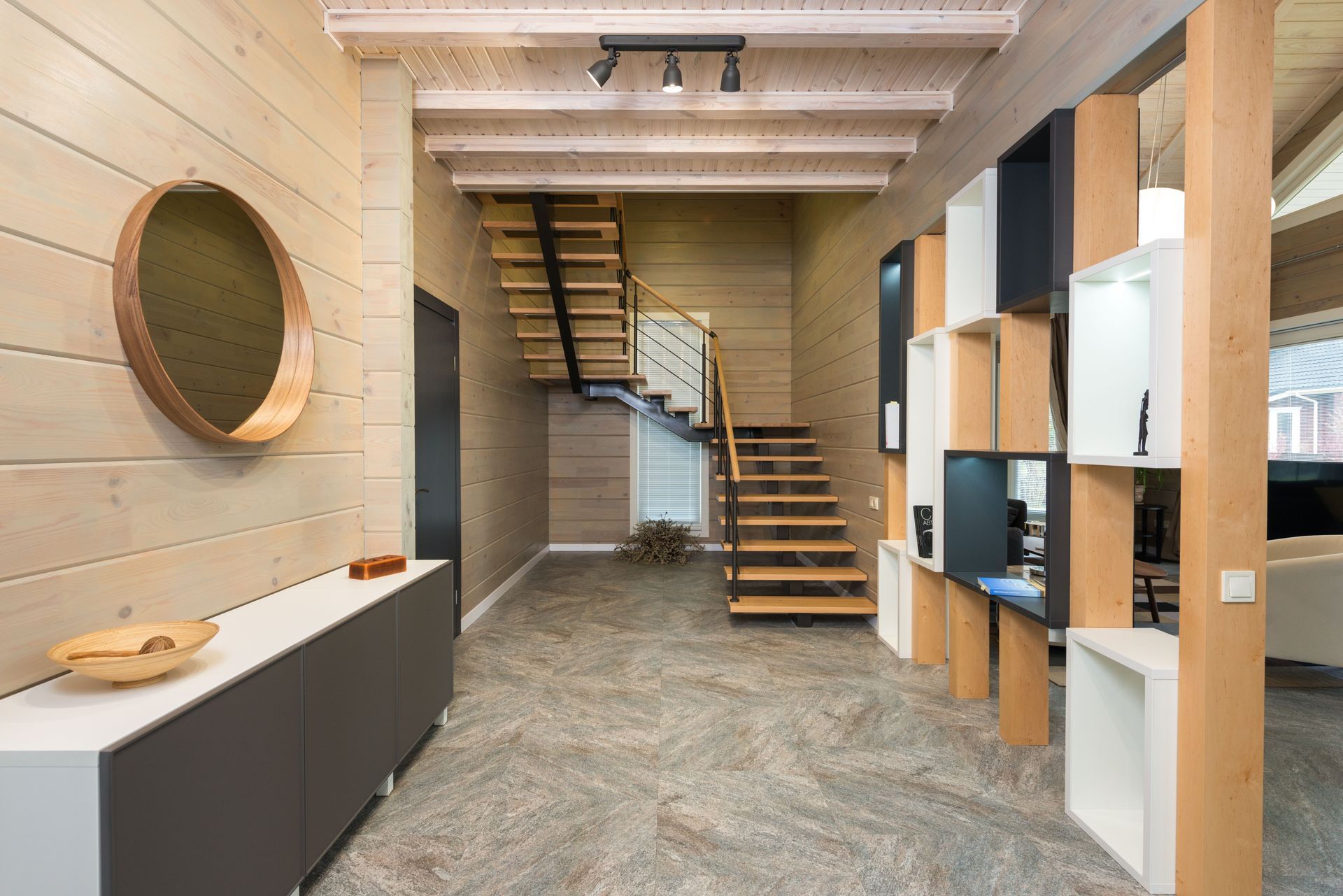 Modern home interior with wood accents, staircase, built-in storage, and a large round mirror