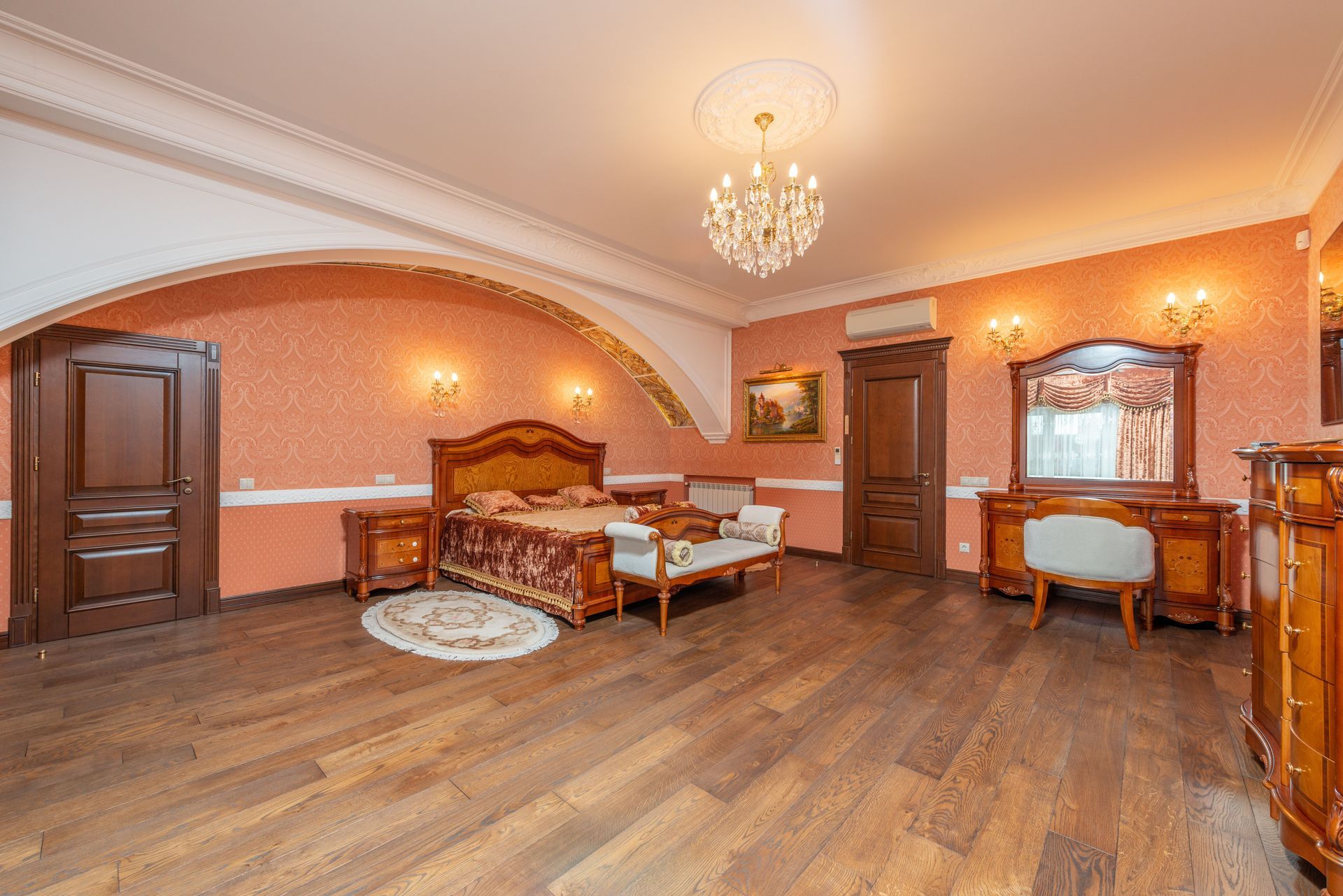 Elegant bedroom with wooden bed, chandelier, mirrored dresser, and warm peach walls