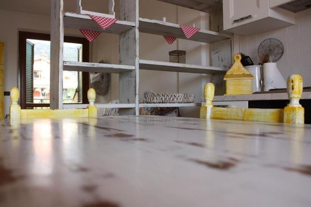 Cucina bianca con tavolo rustico e scaffali aperti, decorata con striscioni triangolari rossi e bianchi.