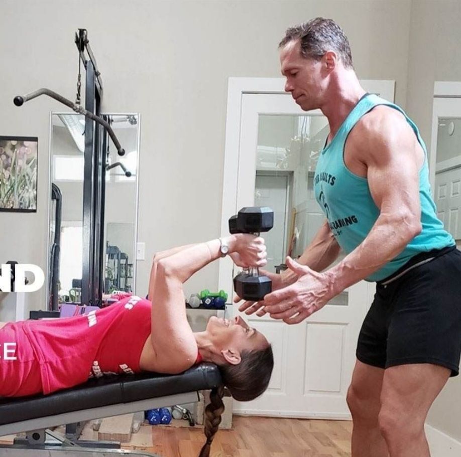 A man is helping a woman lift a dumbbell in a gym