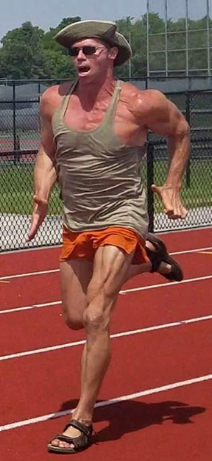 A man in a hat and shorts is running on a track.