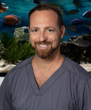 A man in a scrub is smiling in front of a fish tank.