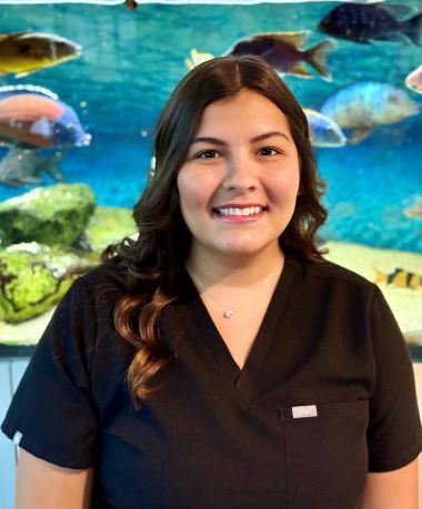 A woman in a black scrub top is smiling in front of a fish tank.