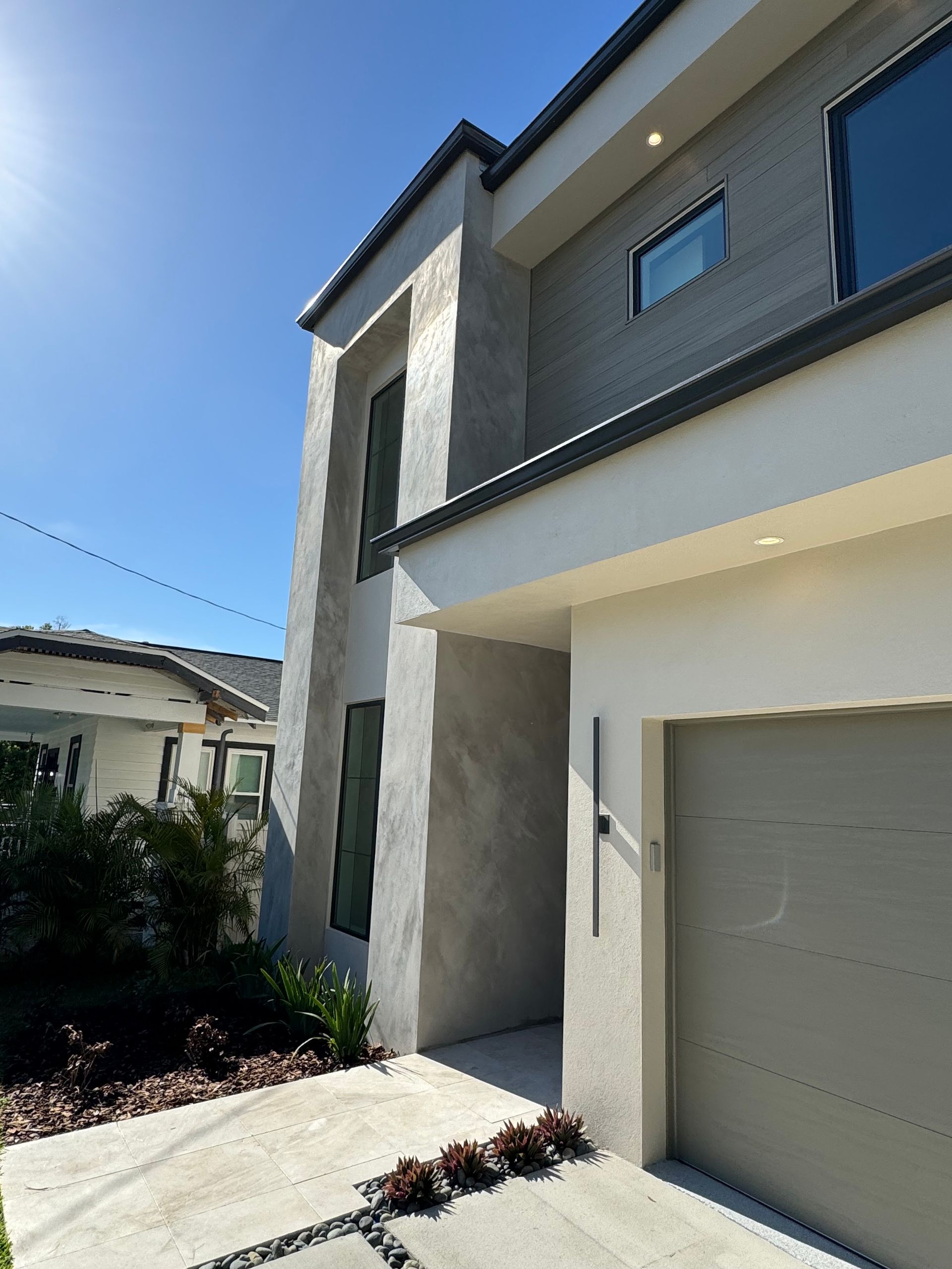 A modern, two-story house exterior featuring a cream-colored garage, gray stone accents, and a paved walkway.