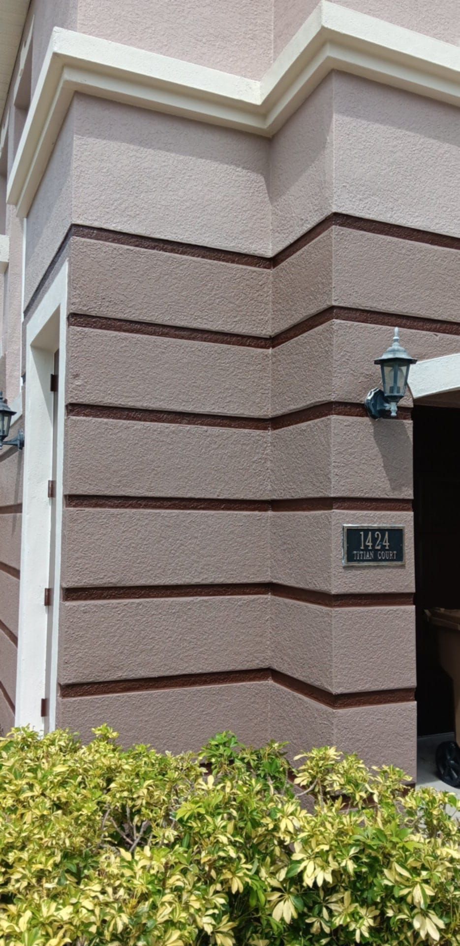 Tan building corner with dark horizontal recessed stripes, a wall lamp, and a sign reading