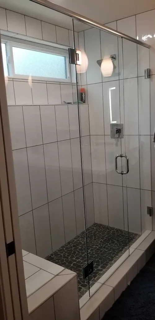 Modern bathroom shower with glass enclosure, handheld showerhead, and pebble-stone floor tile.
