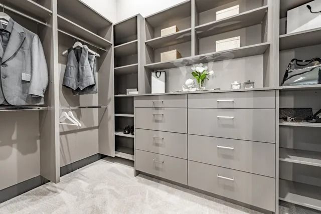 Modern walk-in closet with gray shelving, drawers, hanging clothes, and a light carpeted floor