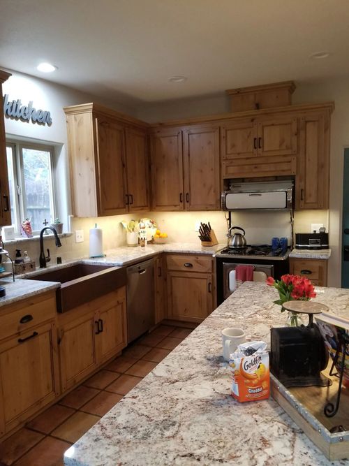 Cozy wood kitchen with granite island, tan cabinets, stainless sink, stove, and flowers on the counter.