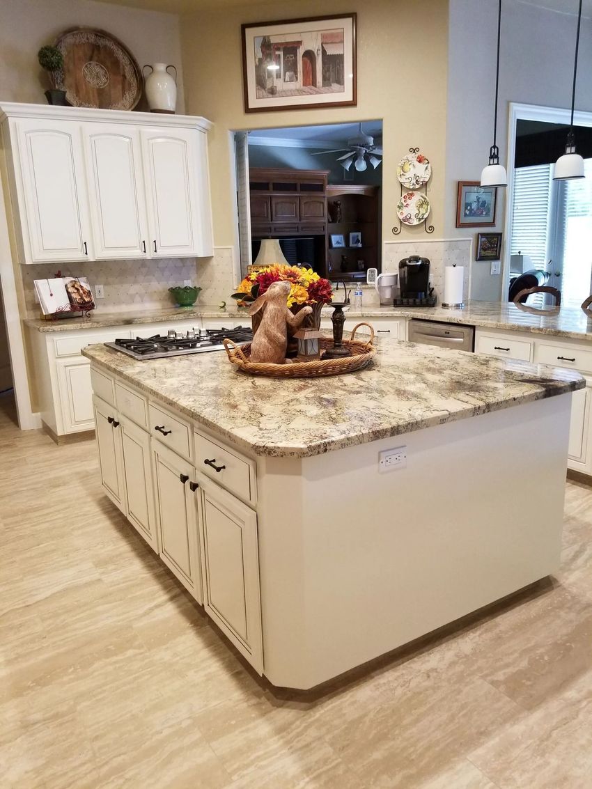 Bright kitchen with a granite island, white cabinets, and decorative centerpiece near a window and doorway.
