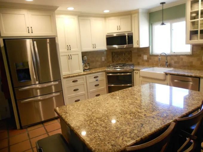 Bright kitchen with granite island, stainless steel appliances, white cabinets, and tiled floor