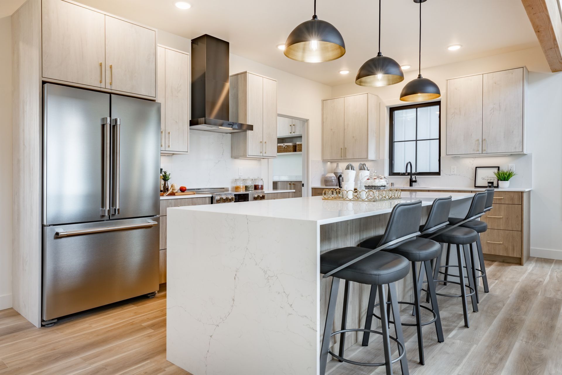 Modern kitchen with stainless-steel appliances, white island, and black bar stools under pendant lights